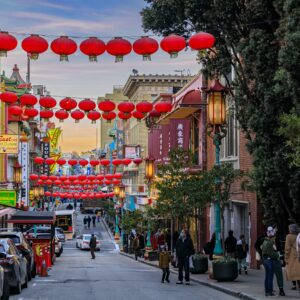 San Francisco, USA - December 18, 2021: Traditional shops, lanterns and people in the street in Chinatown near Downtown with a fiery sunset